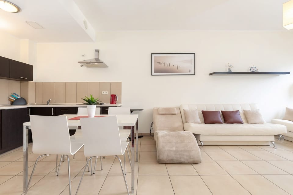 A dining area with a sleek white table and chairs for four, adjacent to a modern kitchen, creating a functional and social cooking and eating space.