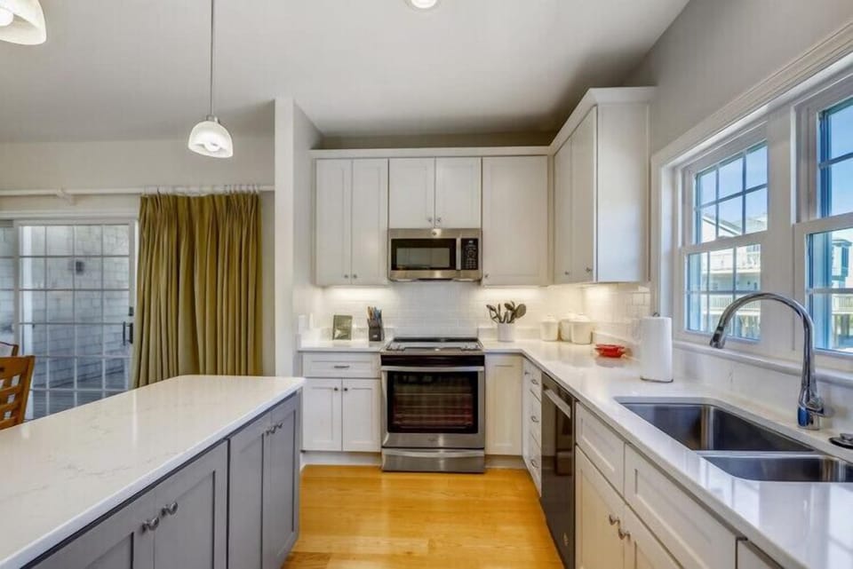 Your bright, modern kitchen features gleaming white counters, stainless-steel appliances, and warm wood floors—perfect for preparing meals and gathering with loved ones during your stay.
