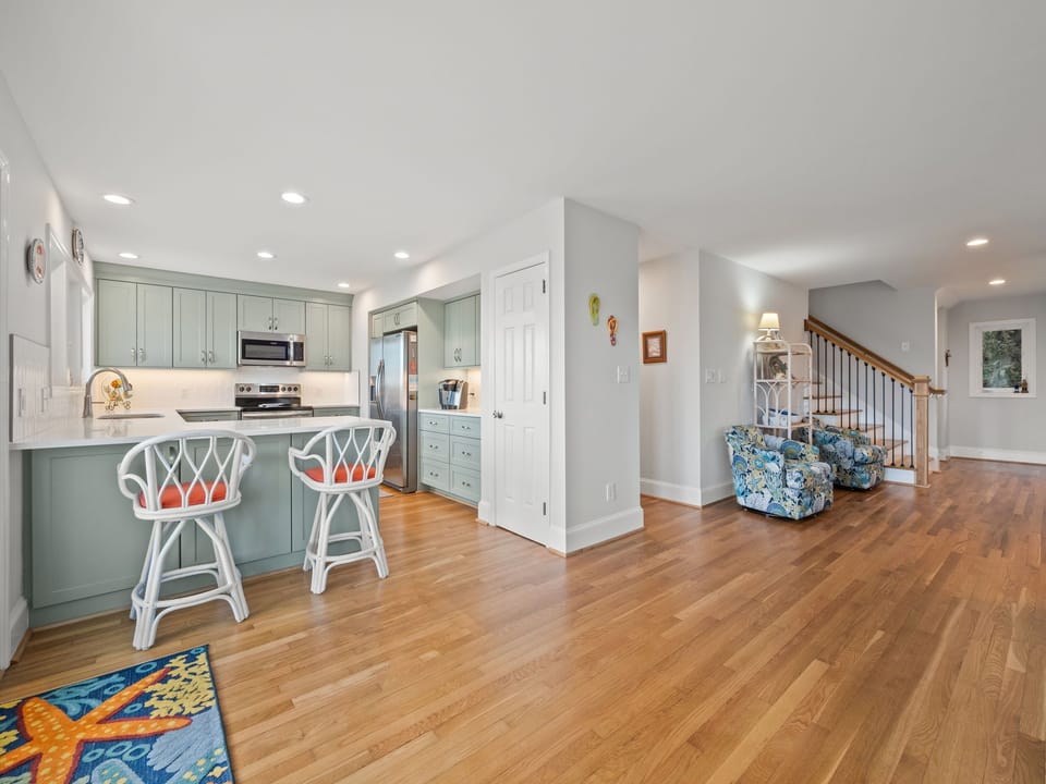 Your open-concept kitchen flows seamlessly into the living area, featuring sage green cabinets and gleaming hardwood floors throughout.