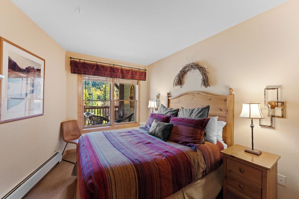 Unwind in your cozy bedroom featuring rustic charm, vibrant linens, and mountain views through your private balcony doors.