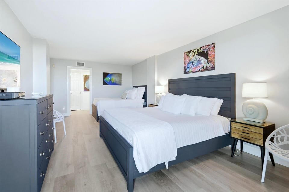Bedroom 1 with one king bed, one queen bed, balcony access, attached bathroom, and 55-inch Smart TV