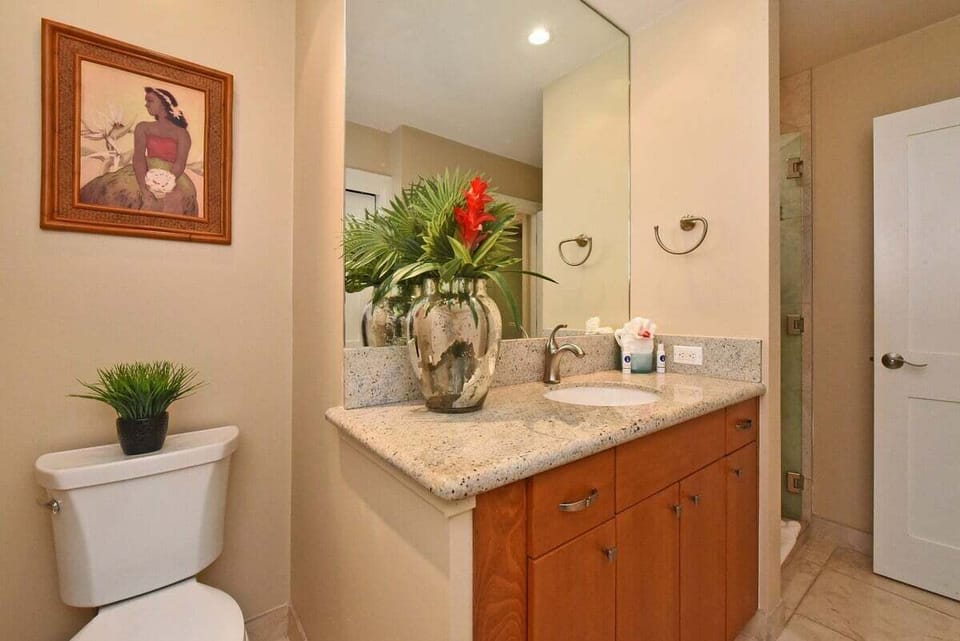 Large en-suite bathroom with dual sinks, granite countertops, ample storage, and bright resort-style lighting.