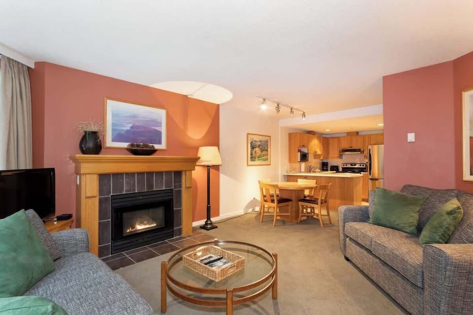 - Inviting living room with fireplace and warm earthy décor  
- Perfect blend of comfort and alpine charm with cozy seating  
- Connect, relax, and enjoy evenings by the glowing firelight  
