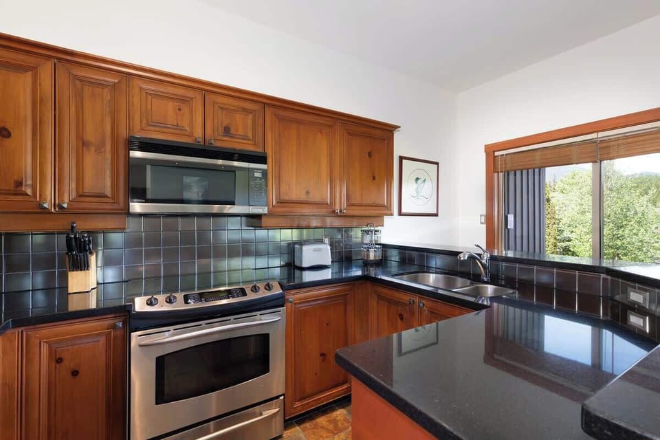 - Fully equipped kitchen with stainless steel appliances and wood cabinets  
- Sleek black countertops and breakfast bar with seating for two  
- Perfect for home-cooked meals after exploring Whistler Village  
