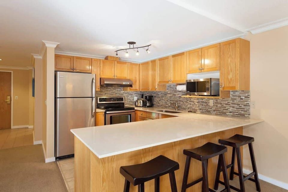 - Modern kitchen with stainless steel appliances and sleek backsplash design  
- Fully equipped for cooking with bar seating perfect for breakfast or après-ski snacks  
- Cozy wood cabinetry adds warmth to this inviting Whistler vacation condo