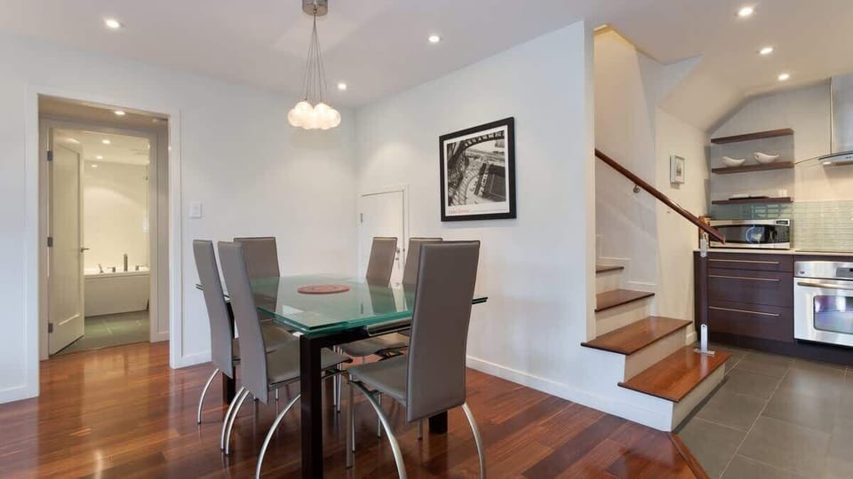 Open dining area w/ a glass table, modern chairs, and easy flow to the kitchen and stairs.