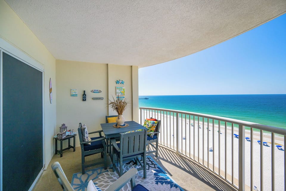 Enjoy a relaxing view from this balcony with wooden seating, colorful cushions, and a vibrant area rug overlooking the beach