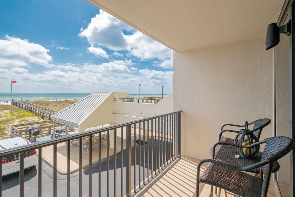 Enjoy a relaxing moment on the balcony with comfortable seating and a scenic view of the beach and vibrant blue skies