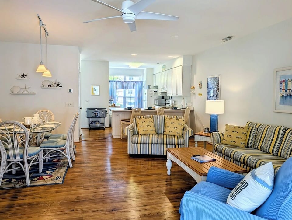 618 Driftwood Court - Sun-Drenched Open Living Area - The main living space features a bright, open layout with high ceilings and warm hardwood-style flooring. A coordinated furniture set with striped patterns and blue accents creates a classic coastal ambiance.