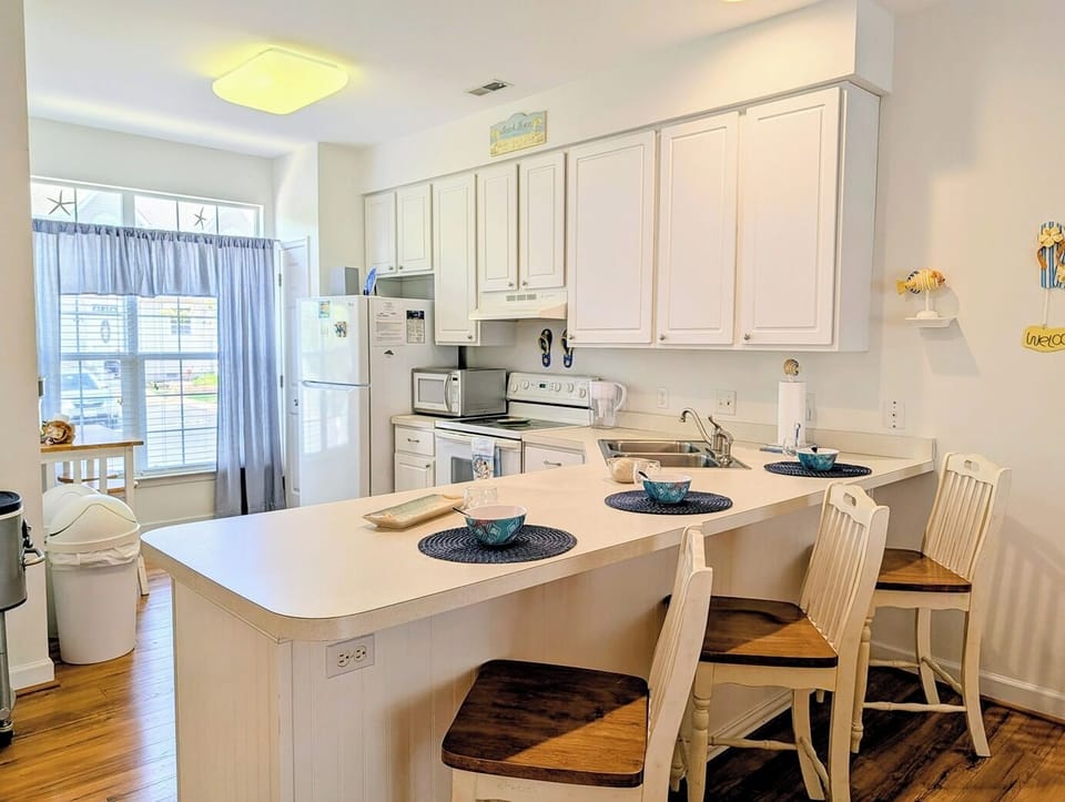 618 Driftwood Court - Gourmet Kitchen with Counter Seating - The kitchen features a long peninsula with white cabinetry and a contrasting dark countertop, offering additional seating for casual meals. Large windows in the adjacent dining area flood the entire space with natural light.