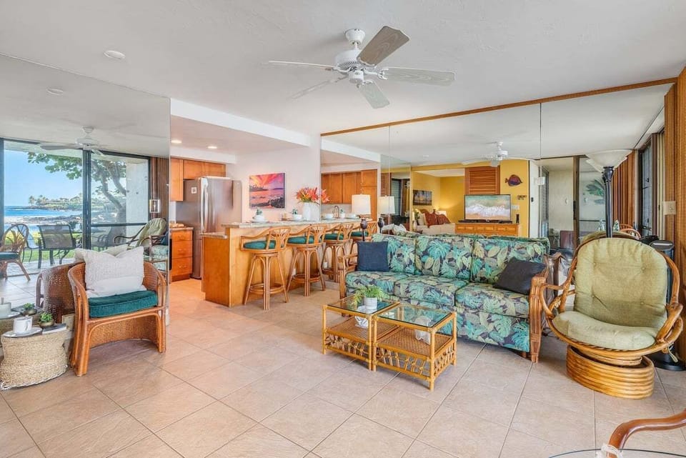 Enjoy a wide open living layout filled with natural light, rattan furnishings, and direct views toward the oceanfront lanai