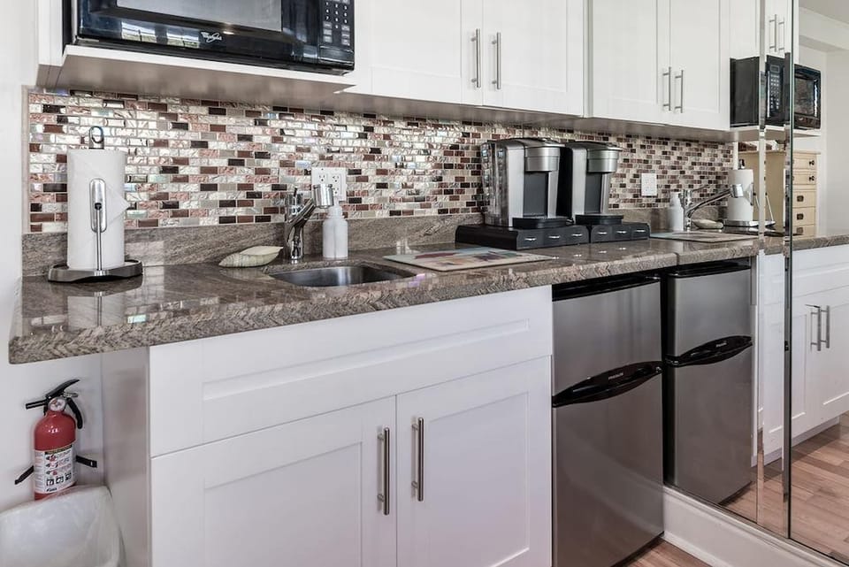 Kitchenette with a Toaster oven, microwave, mini fridge, Keurig coffee maker, glasses, plates, and cutlery. 