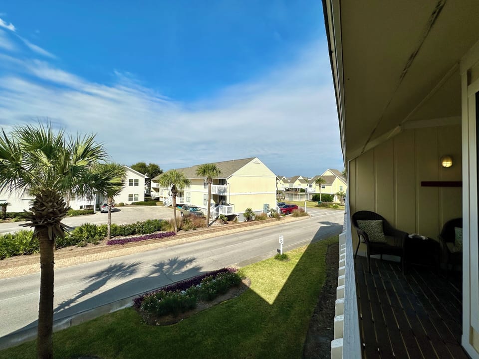 Relax on your private balcony with comfortable seating while enjoying peaceful neighborhood views and palm trees swaying in the coastal breeze.