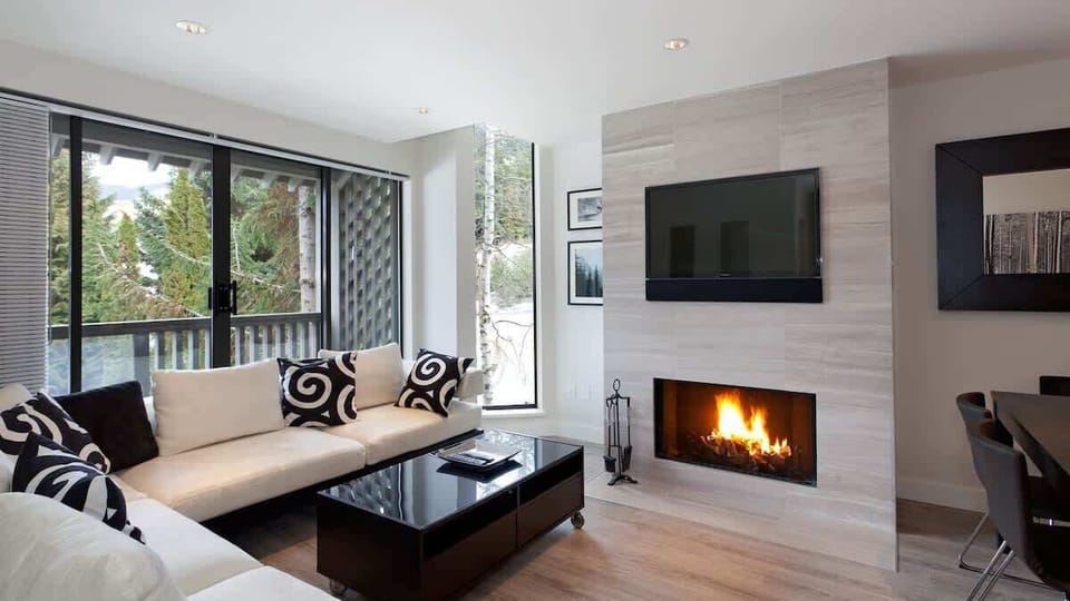 - Bright living area with sleek fireplace and large windows framing forest views  
- Plush sectional seating ideal for après-ski relaxation and movie nights  
- Modern design blending comfort with warm mountain charm