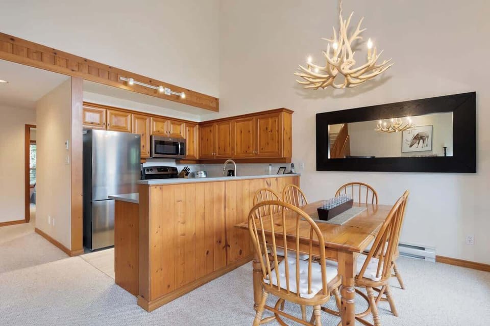 - Cozy dining area with wooden table and antler chandelier creating warm mountain charm  
- Bright windows showcase peaceful forest views while enjoying meals with loved ones  
- Connected to the kitchen and living area for easy entertaining