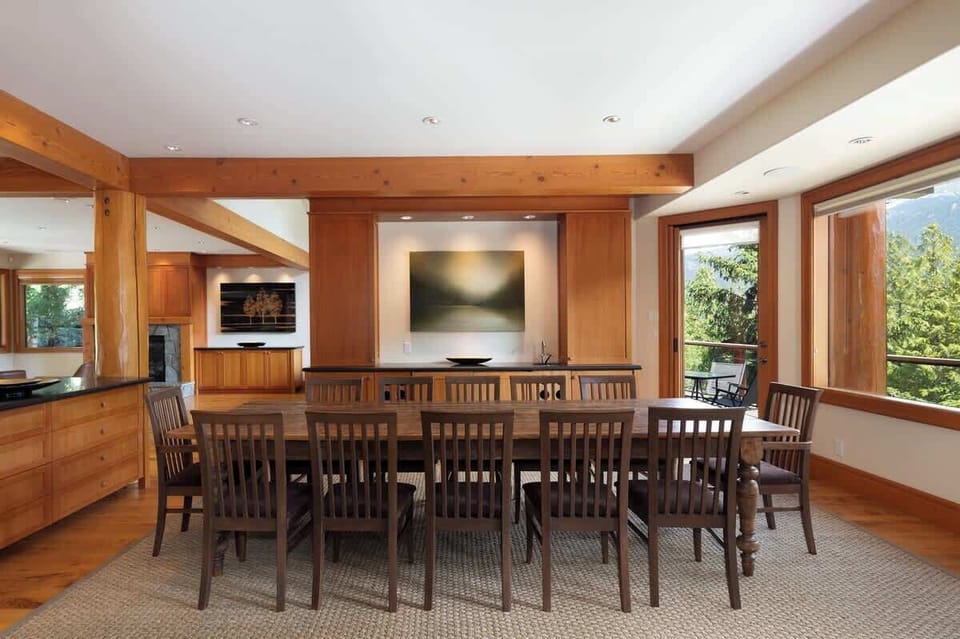 - Long dining table framed by windows capturing forest and slope views  
- Warm wood tones and soft lighting create an inviting mountain ambiance  
- Perfect for shared meals, laughter, and scenic alpine moments  
