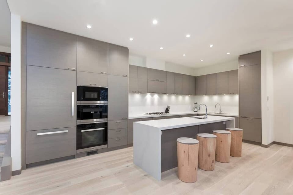 - Sleek modern kitchen with high-end appliances and soft gray cabinetry  
- Large island with natural wood stools and elegant lighting  
- Fully equipped space for cooking and gathering with loved ones  