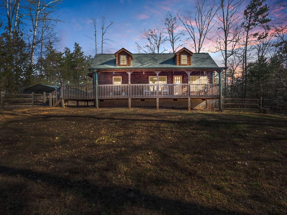 Charming log cabin with a spacious deck, perfect for enjoying serene forest views at sunset.