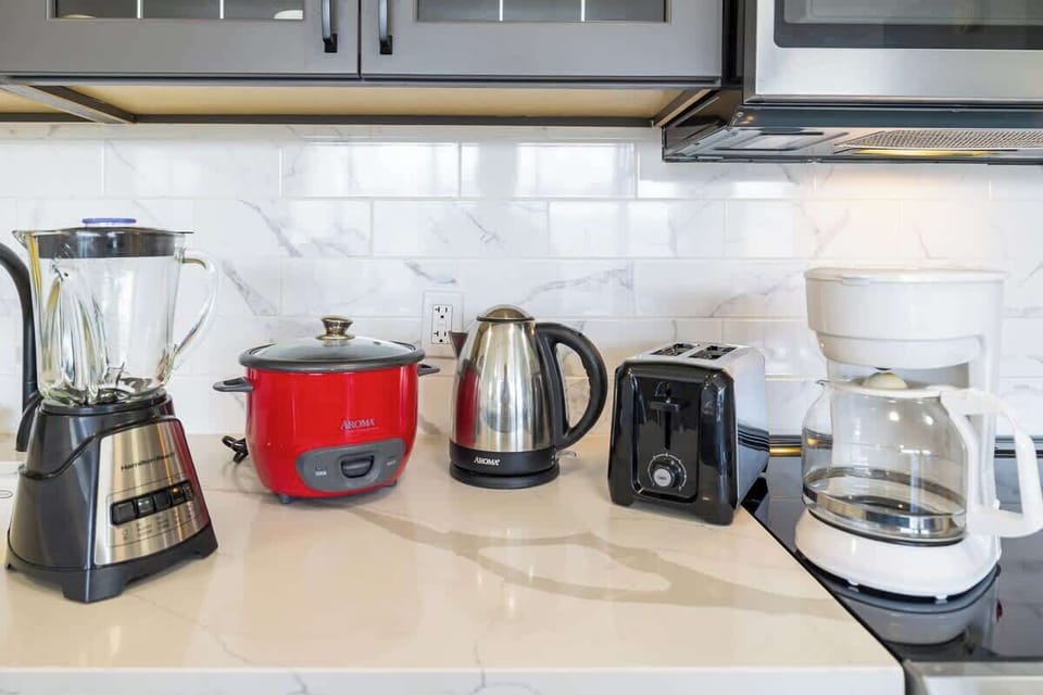 Modern kitchen countertop with essential appliances including a blender, rice cooker, electric kettle, toaster, and coffee maker.