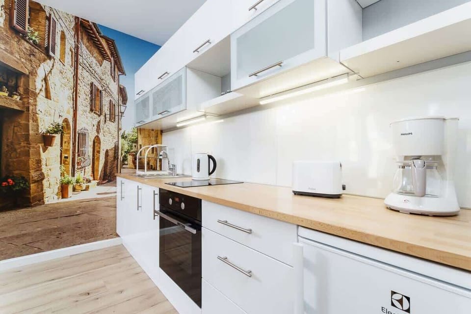 A bright kitchen with white countertops, cabinets, and wooden finishes, with a window in the background.