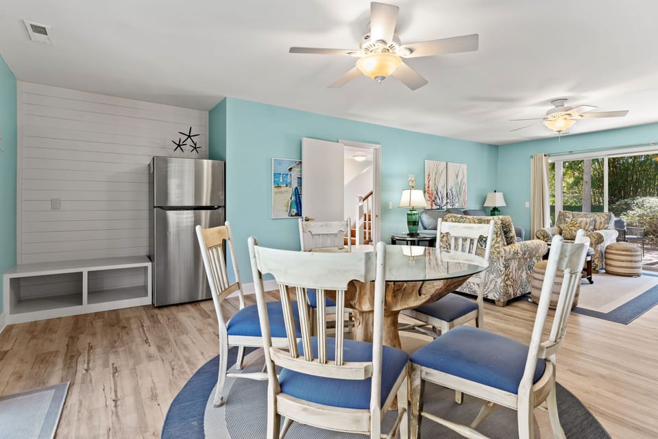 Downstairs living room with queen sleeper sofa, large smart TV, sliders leading to front yard and backyard, dining table and refrigerator