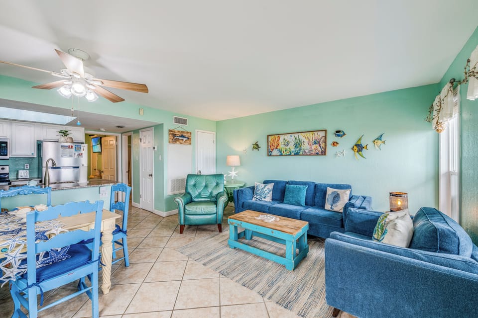 Relax in your coastal-themed living room with ocean-inspired decor, comfortable blue seating, and an open kitchen for easy entertaining.