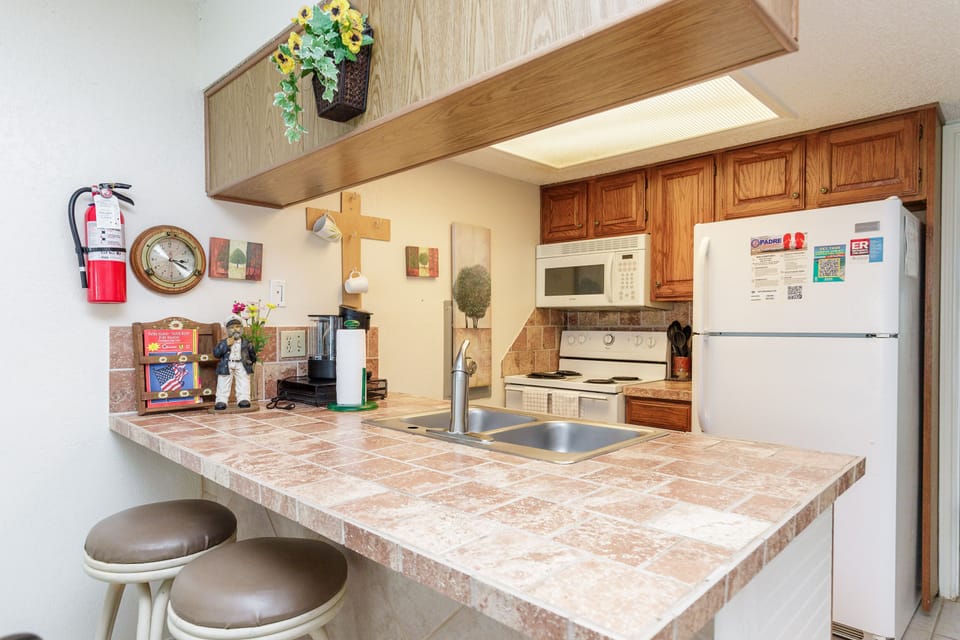 Your fully-equipped kitchen awaits with warm wood cabinets, modern appliances, and cozy breakfast bar seating for morning coffee.