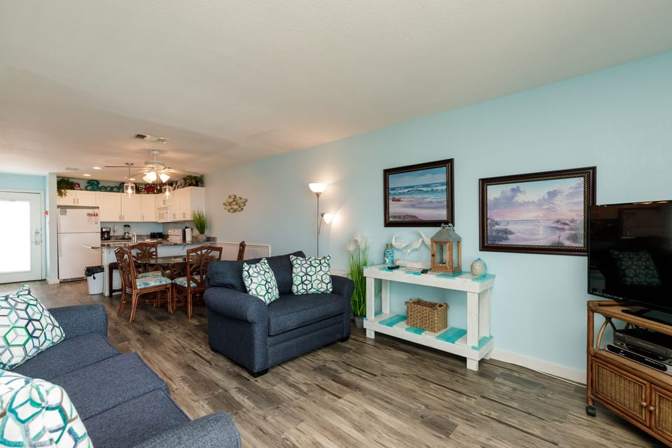 Relax in your coastal-themed living space featuring comfy navy sofas and beachside artwork that sets the perfect vacation mood.