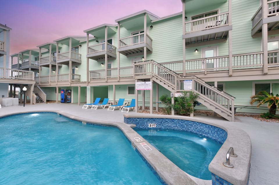 Charming beachside property with mint green buildings featuring multi-level balconies and a relaxing pool area at twilight.