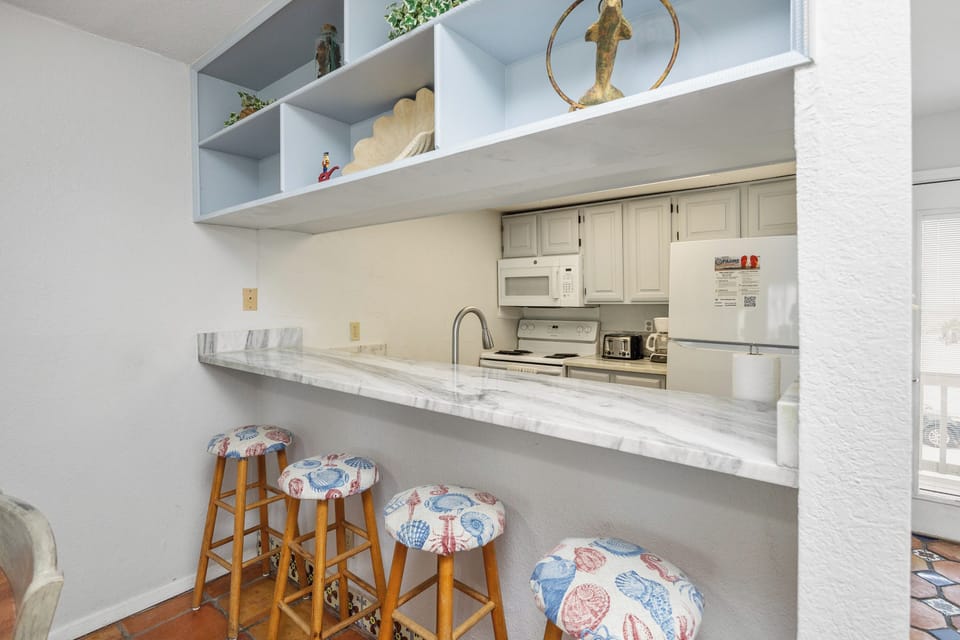 Your fully equipped kitchen features a breakfast bar with coastal-themed seating, perfect for morning coffee or casual dining together.