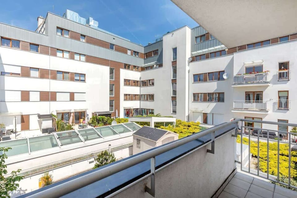 A balcony view showing the surrounding modern apartment buildings with greenery and bright outdoor lighting.