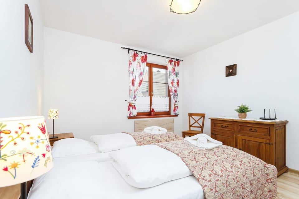 Bedroom with two single beds, floral curtains, and a small bedside table. Wall art adds a cozy touch.