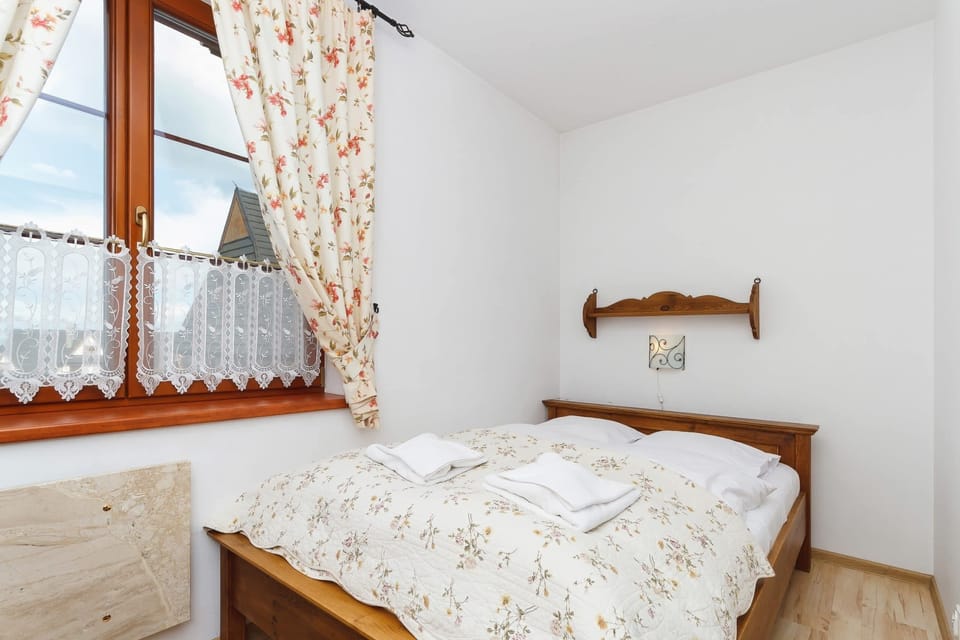 A bedroom with double bed placed side by side, floral curtains, and a window offering a view of the mountains.