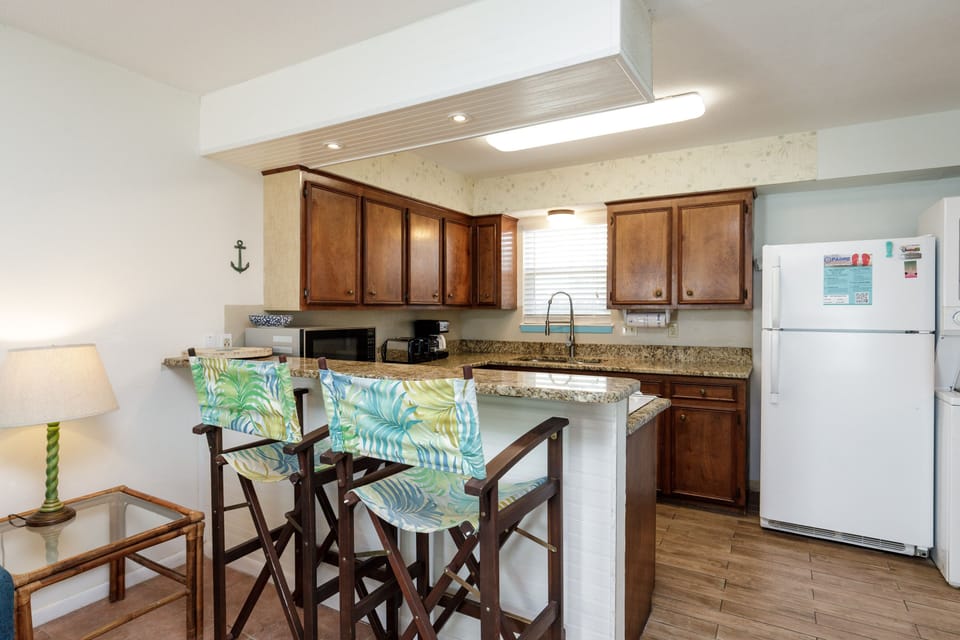 Your fully-equipped kitchen awaits with warm wood cabinets, granite counters, and tropical-themed seating perfect for morning coffee or casual meals.
