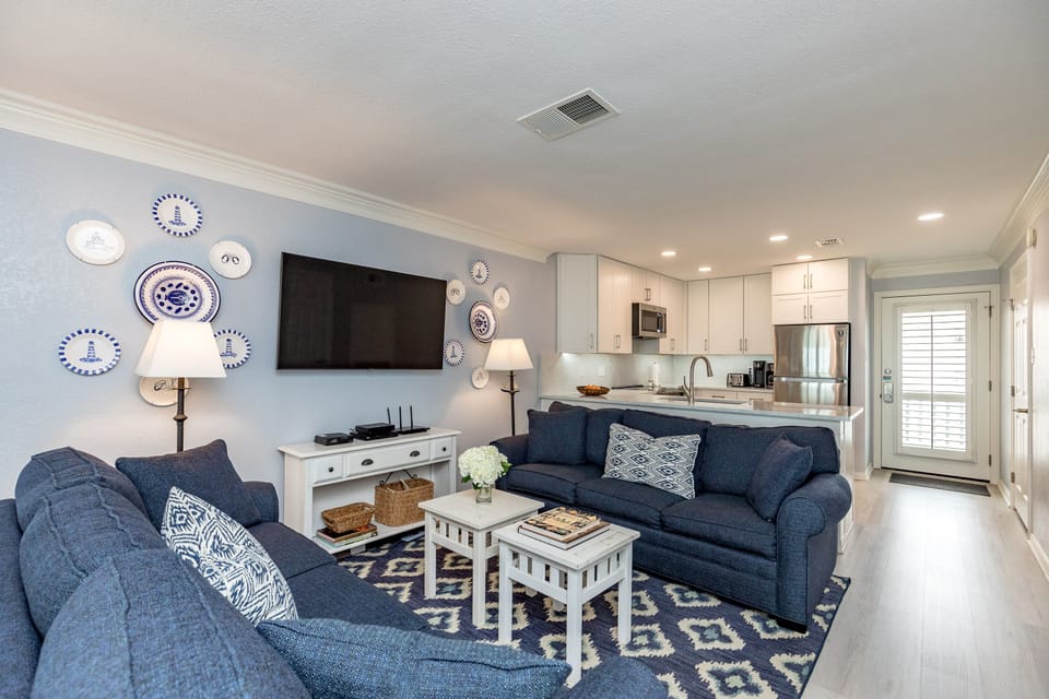 Relax in your beautifully appointed living space featuring comfortable navy seating, charming coastal décor, and a fully equipped kitchen perfect for home-cooked meals.