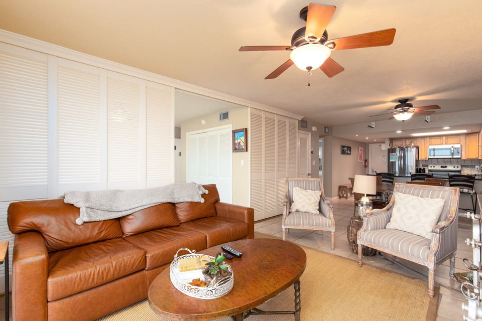 Relax in your spacious living area with comfortable leather seating, ceiling fans, and an open layout connecting to the modern kitchen.