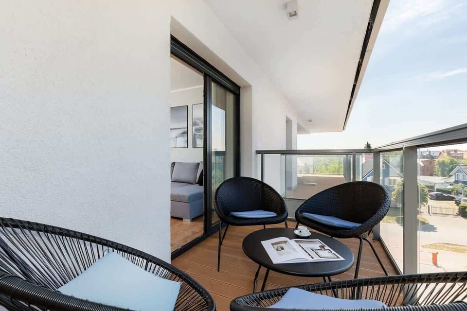 A balcony view with two black lounge chairs and a glass railing, overlooking the surrounding area.