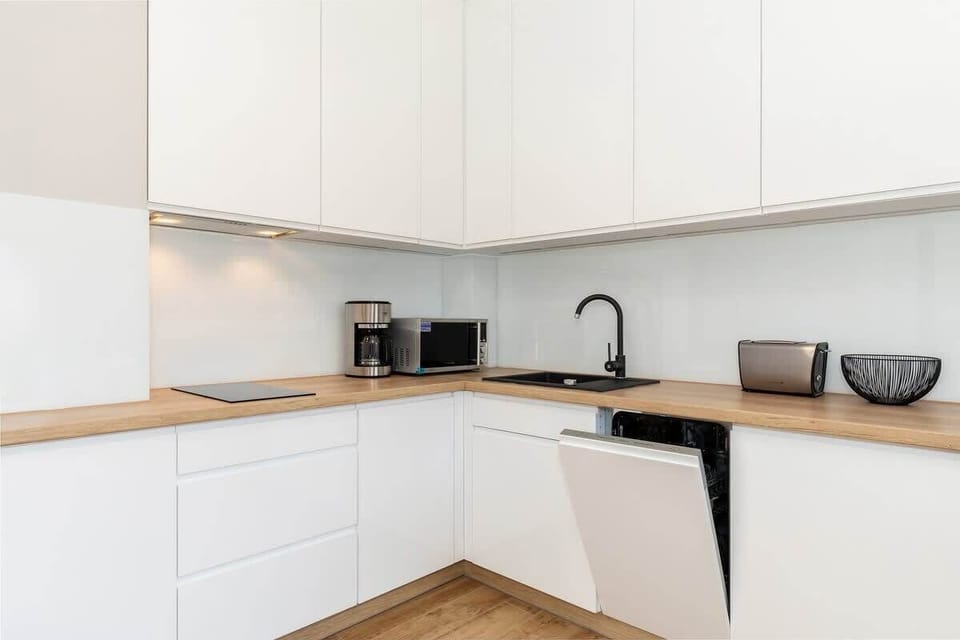 A compact, modern kitchen with sleek white cabinets, a built-in sink, and minimalistic design, accented by light wood.