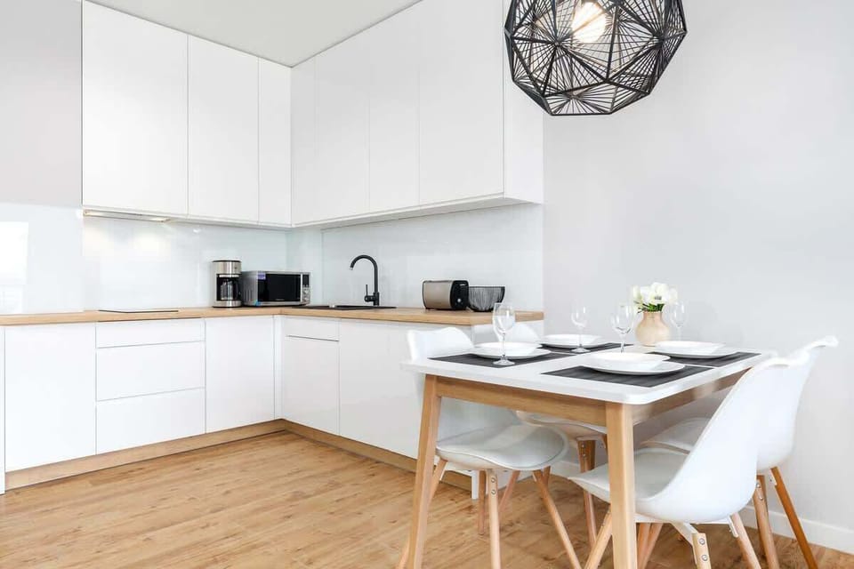 A sleek kitchenette with white cabinets and a wooden countertop, connected to a dining area with a round table and white chairs.