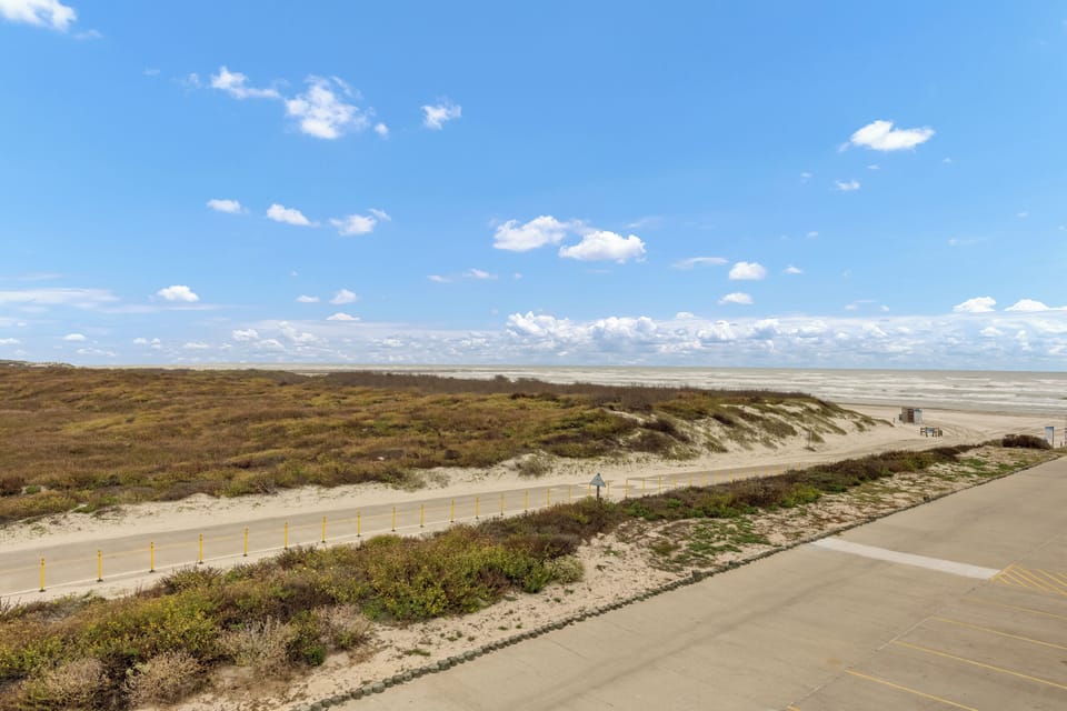 Coastal dunes and beach access area with natural vegetation and sandy pathways leading to the shoreline.