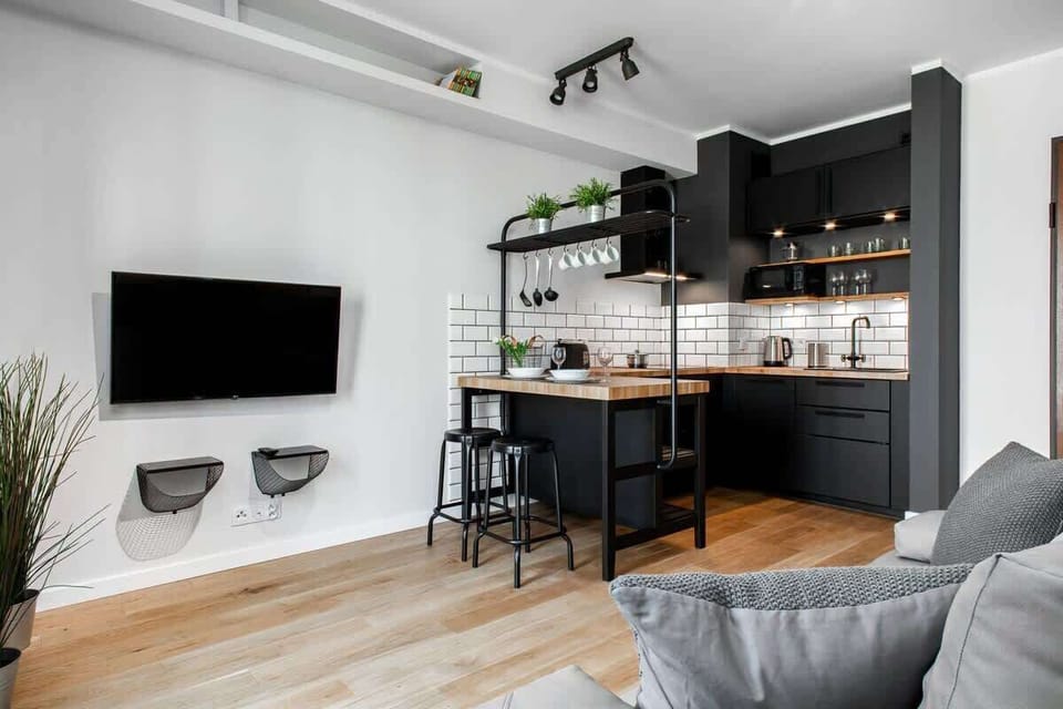 A spacious living room with a large couch facing a wall-mounted TV. There are open shelves on the wall, and the design feels modern with an industrial touch.