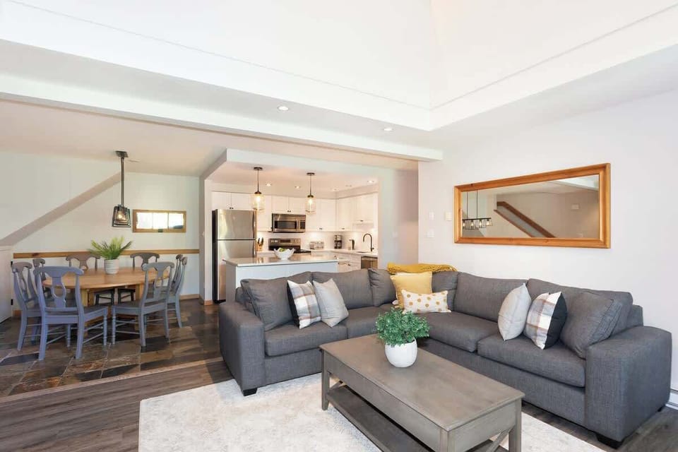 - Bright open living room with plush sofas and wide windows  
- Mirror and natural light create a welcoming airy feel  
- Relax with forest views after your Whistler day adventures  
