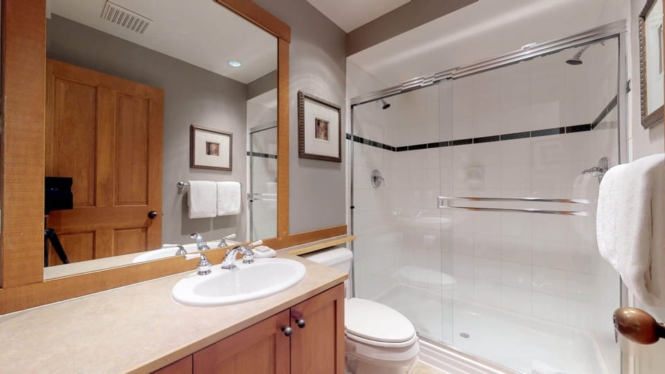 - Bright bathroom with glass shower and wooden vanity design  
- Clean modern space with soft lighting and warm details  
- Perfect for refreshing after a day exploring Whistler trails  
