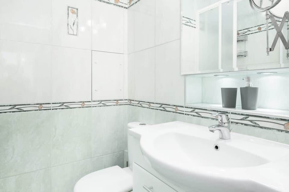  A bathroom sink area with white tiles and a small ledge holding toiletries. The design is clean and minimalistic.