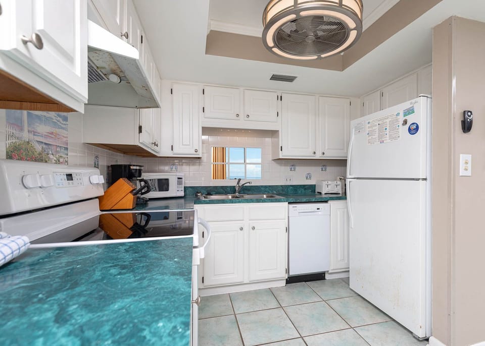 Bright kitchen featuring white cabinets, white appliances, and a sink mirror showcasing the lovely balcony view