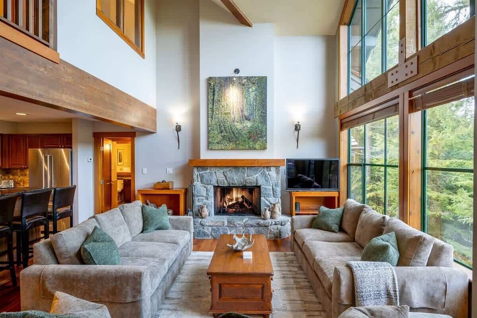 - Cozy living room with high vaulted ceilings and tall windows  
- Stone fireplace centerpiece adds warmth and mountain charm  
- Plush sofas offer space to relax and enjoy forest views  
