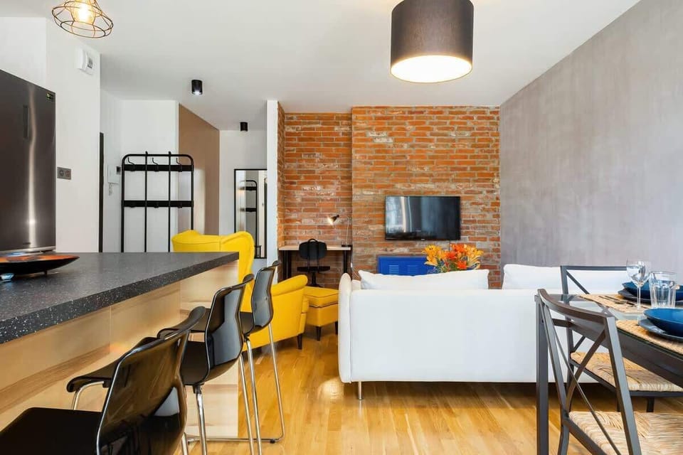 A stylish living room with exposed brick walls, bright yellow furniture, and a white coffee table adorned with vibrant flowers, creating a trendy, welcoming vibe.