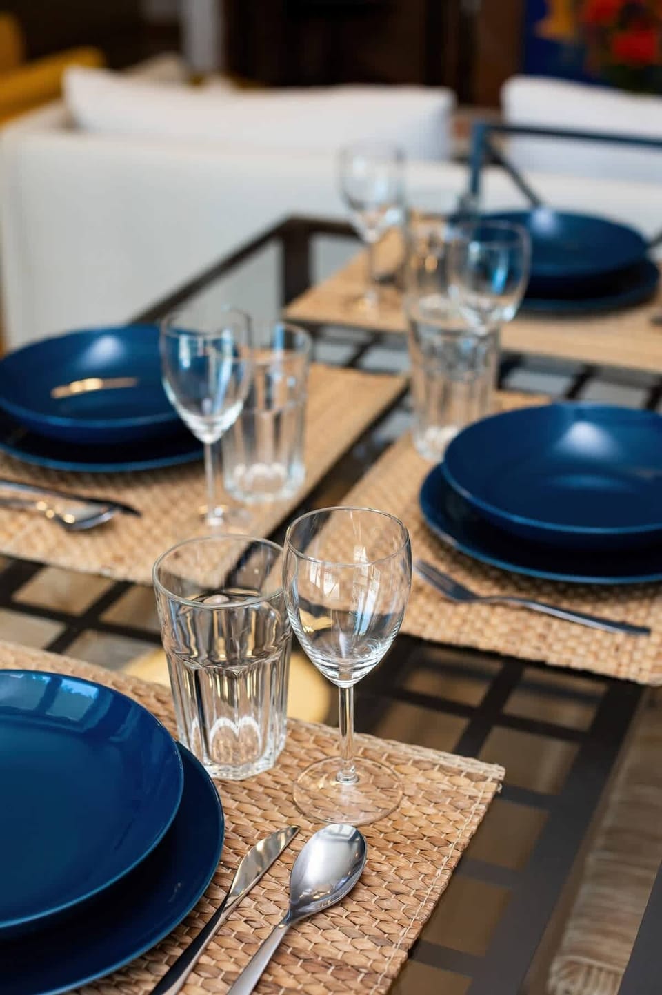 A dining area with a table set elegantly with dark blue plates and glassware, framed by a cozy yet modern open-plan living space.