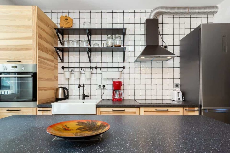A modern kitchen with a rustic touch, featuring wooden cabinetry, open shelving, and a tiled backsplash, with a sleek countertop and hanging lights.
