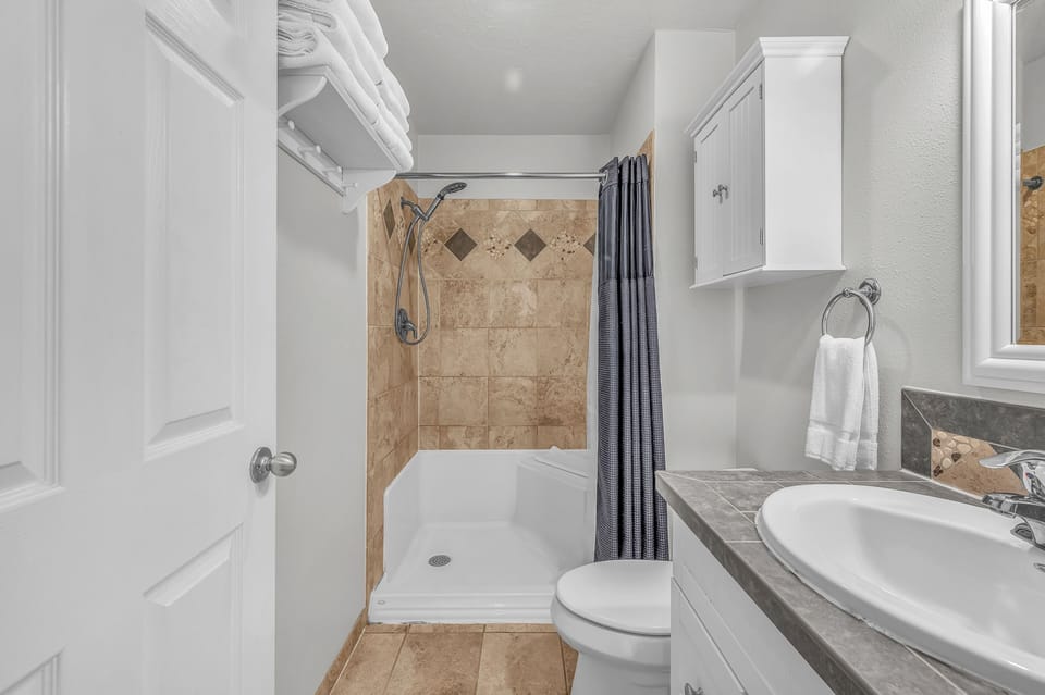 Step into your pristine bathroom with natural stone details, crisp white linens, and a refreshing walk-in shower.